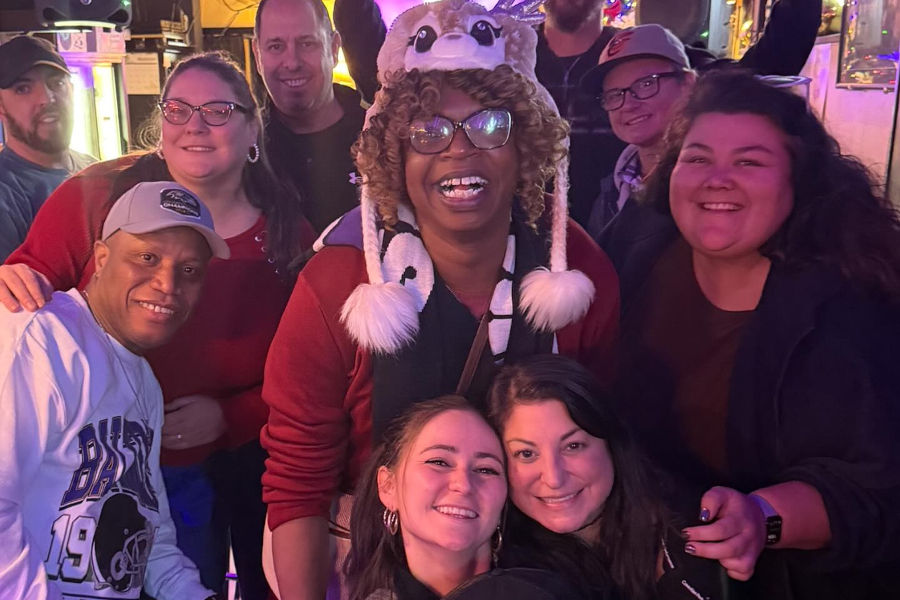 Indoor bar scene with joyful regulars posing for a reunion photo under purple lights.
