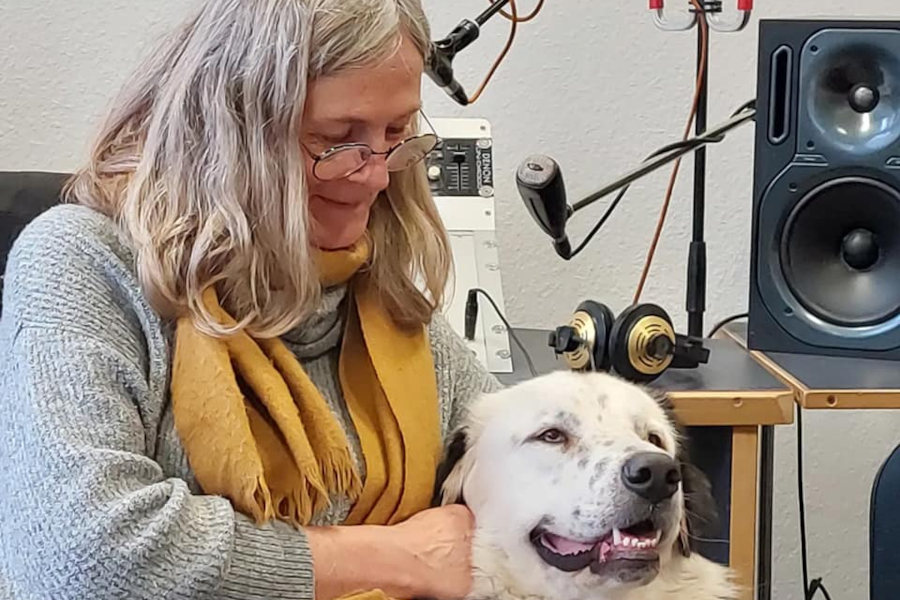 Janka Kluge sitting in a radio studio, gently holding a white dog on her lap.