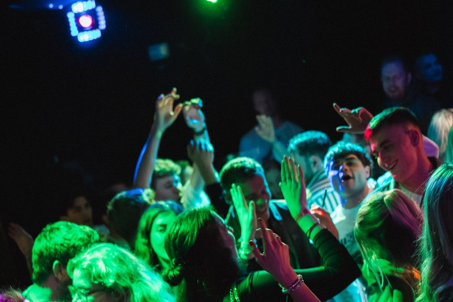 Colorful crowd dancing under green and purple lights at Rauschgold bar in Berlin.