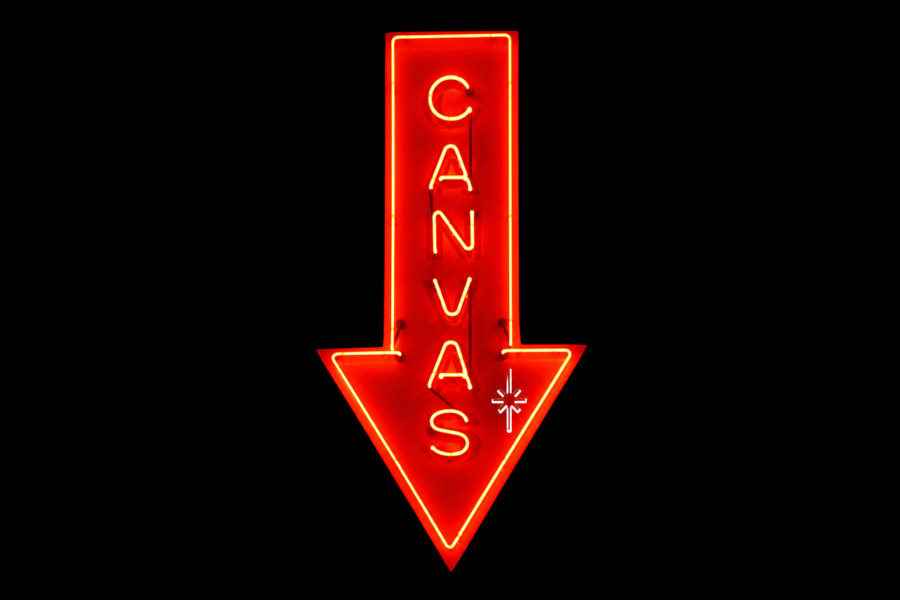 Bright red neon sign for Canvas Lounge shaped like a downward arrow, displaying the venue’s name on a black background.