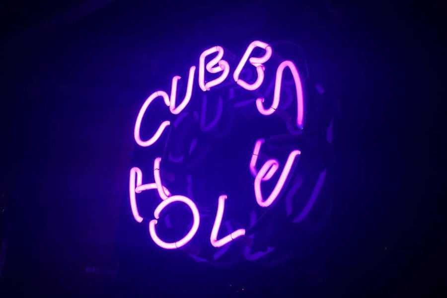 Neon sign reading Cubbyhole glowing in purple light.