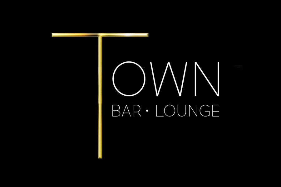 Logo of Town Bar & Lounge featuring an elongated gold T beside the venue name written in thin white capital letters.
