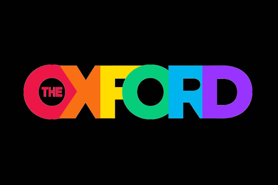 Logo of The Oxford Hotel displaying large rainbow-colored “OXFORD” text with “THE” inside the O on a black background.