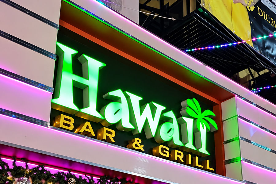 Exterior of Hawaii Bar & Grill in Tijuana with a large green sign and pink and multicoloured lights across the façade.